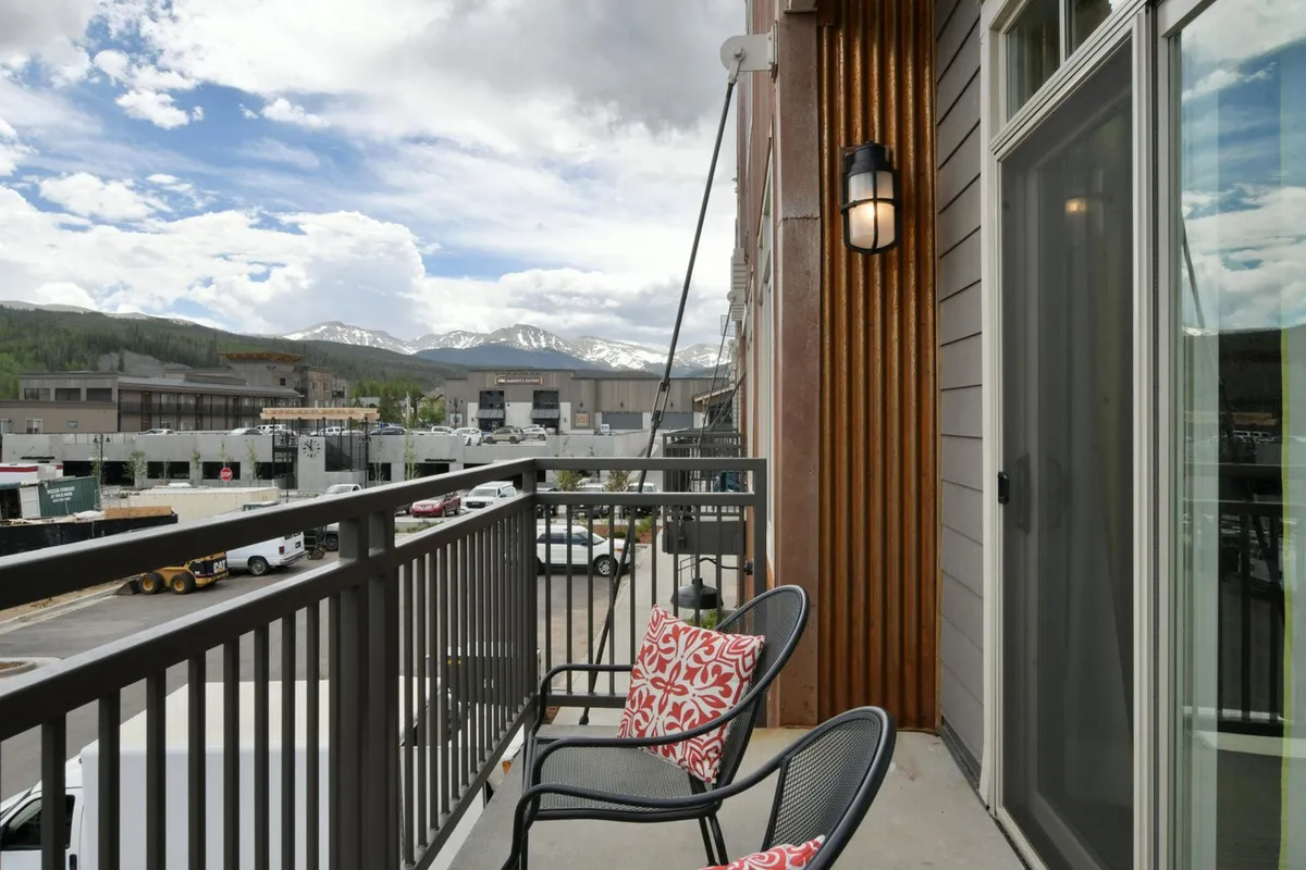 This image features a balcony seating area with comfortable outdoor furniture overlooking a breathtaking mountain view. The exterior wall texture and the open sky add to the sense of openness and tranquility, perfectly evoking the feeling of an indoor/outdoor living experience.