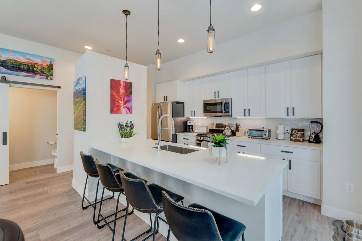 A modern, open kitchen with a central island lined with bar stools, sleek stainless steel appliances, and vibrant wall art. The layout invites conversation and shared culinary experiences, ideal for casual meals or festive occasions.
